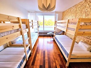Ein Schlafsaalzimmer mit Etagenbetten, Holzboden und einem großen Fenster mit Blick auf Grünflächen.
