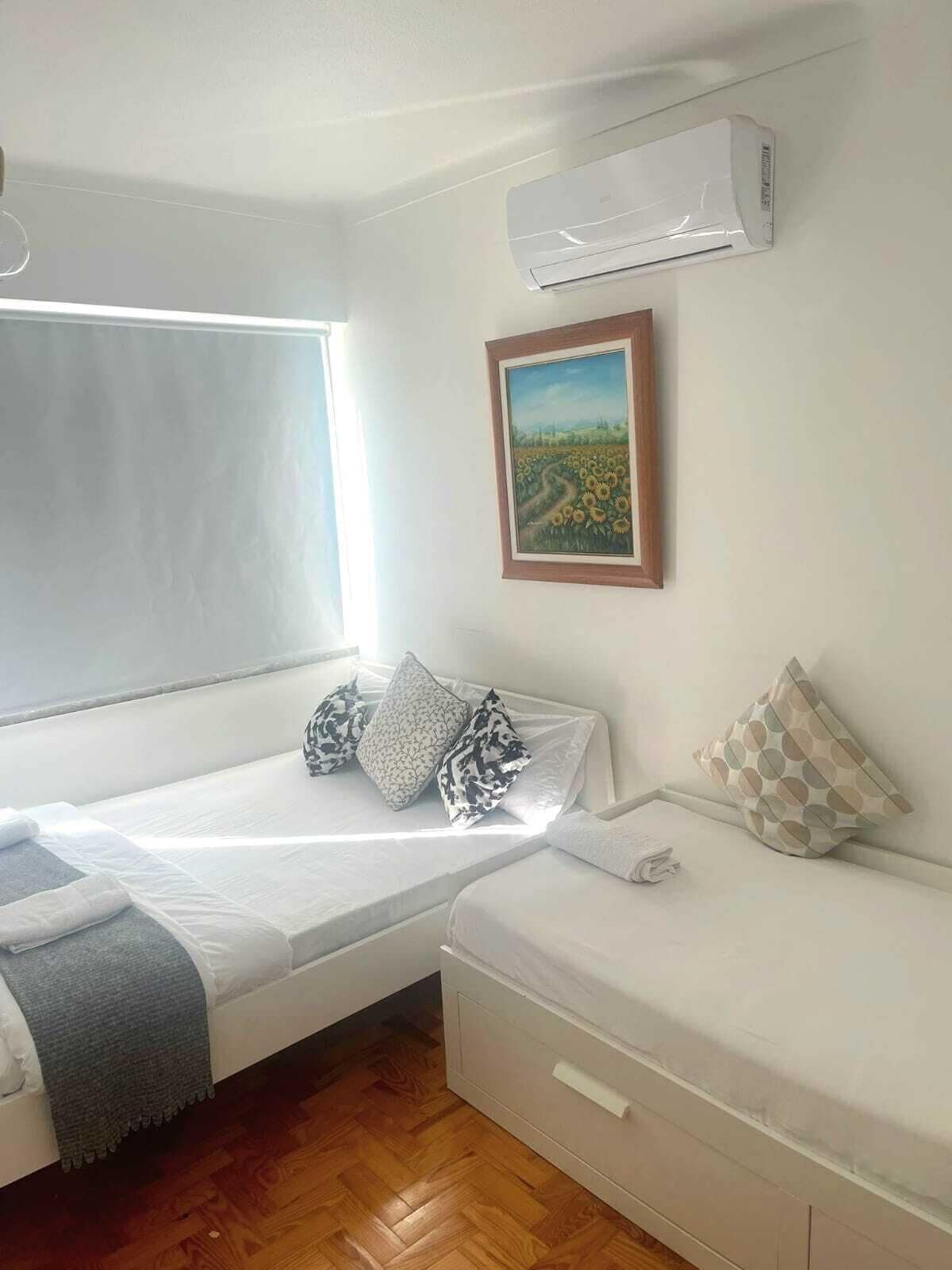 Una habitació amb un llit, una finestra, un aparell d'aire condicionat i un quadre a la paret.