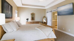 A bedroom with a large bed, a ceiling fan, a dresser, a mirror, and a TV.