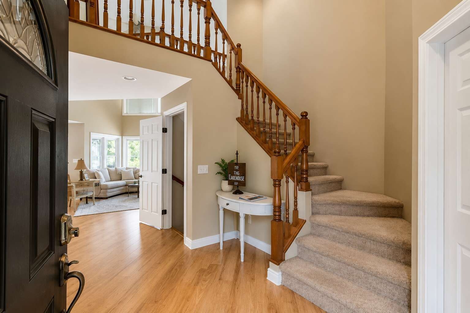 A home interior with a wooden staircase, a white door, and a living room with a sofa and a table.