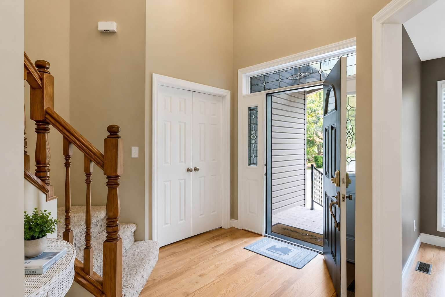 A hallway with a wooden staircase, a white door, and a glass door leading outside.