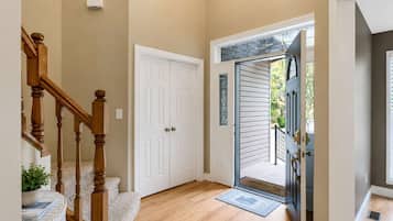 A hallway with a wooden staircase, a white door, and a glass door leading outside.