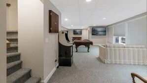 A home interior with a staircase, a pool table, a sofa, and two wall-mounted TVs.