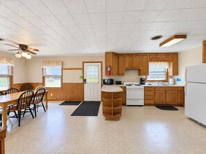 A kitchen with wooden cabinets, a stove, a refrigerator, and a dining area with a table and chairs. - Cedar Cove Cabin 1 (Butternut)