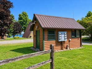 A small wooden cabin with a sloped roof, a green door, and a utility box. - Cedar Cove Cabin 1 (Butternut)