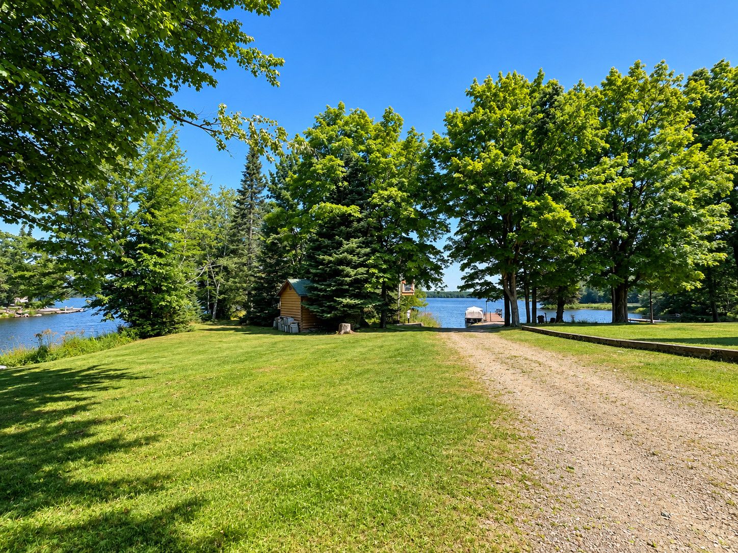 A grassy area with a small wooden cabin and a gravel path leading to a body of water.