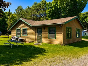 Ein kleines Blockhaus mit grüner Tür und Fenstern, einem Picknicktisch und einem Grill vor der Tür.