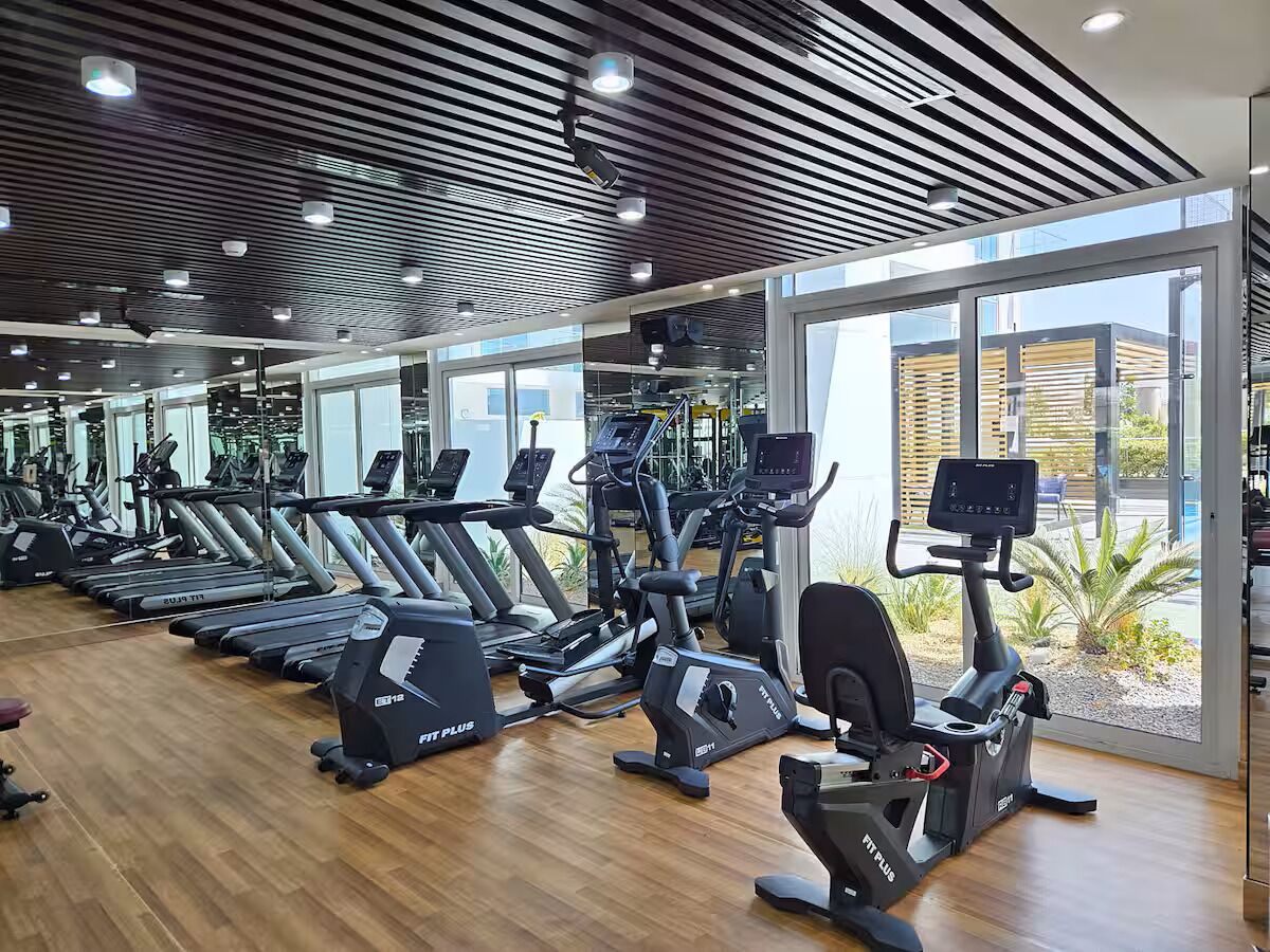 Un gimnasio con cintas de correr, elípticas y bicicletas estáticas, amplias ventanas y suelo de madera.