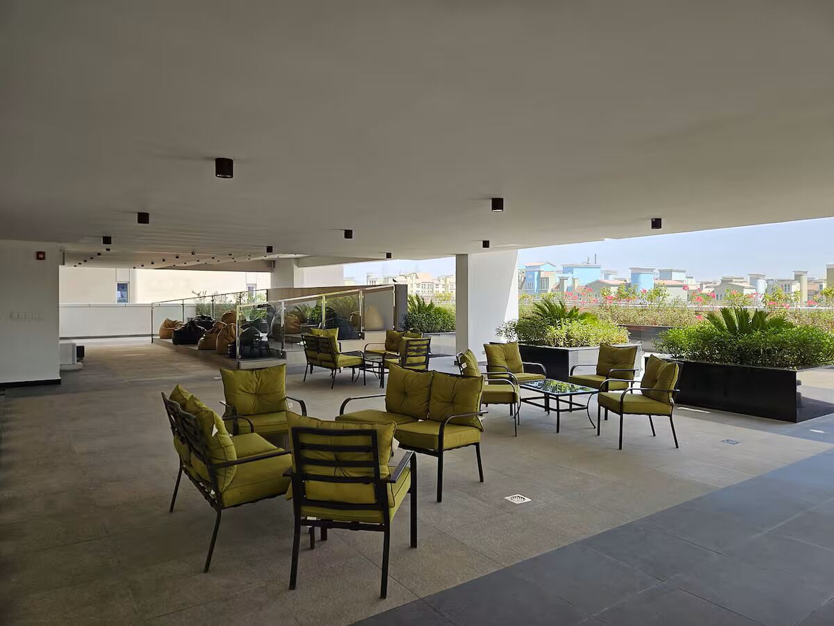 An outdoor seating area with yellow chairs and tables, surrounded by plants and a city view.