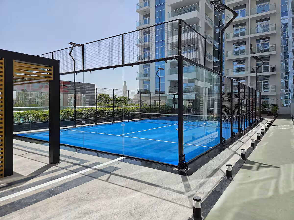 A rooftop tennis court with a net, surrounded by glass railings and a modern building in the background.