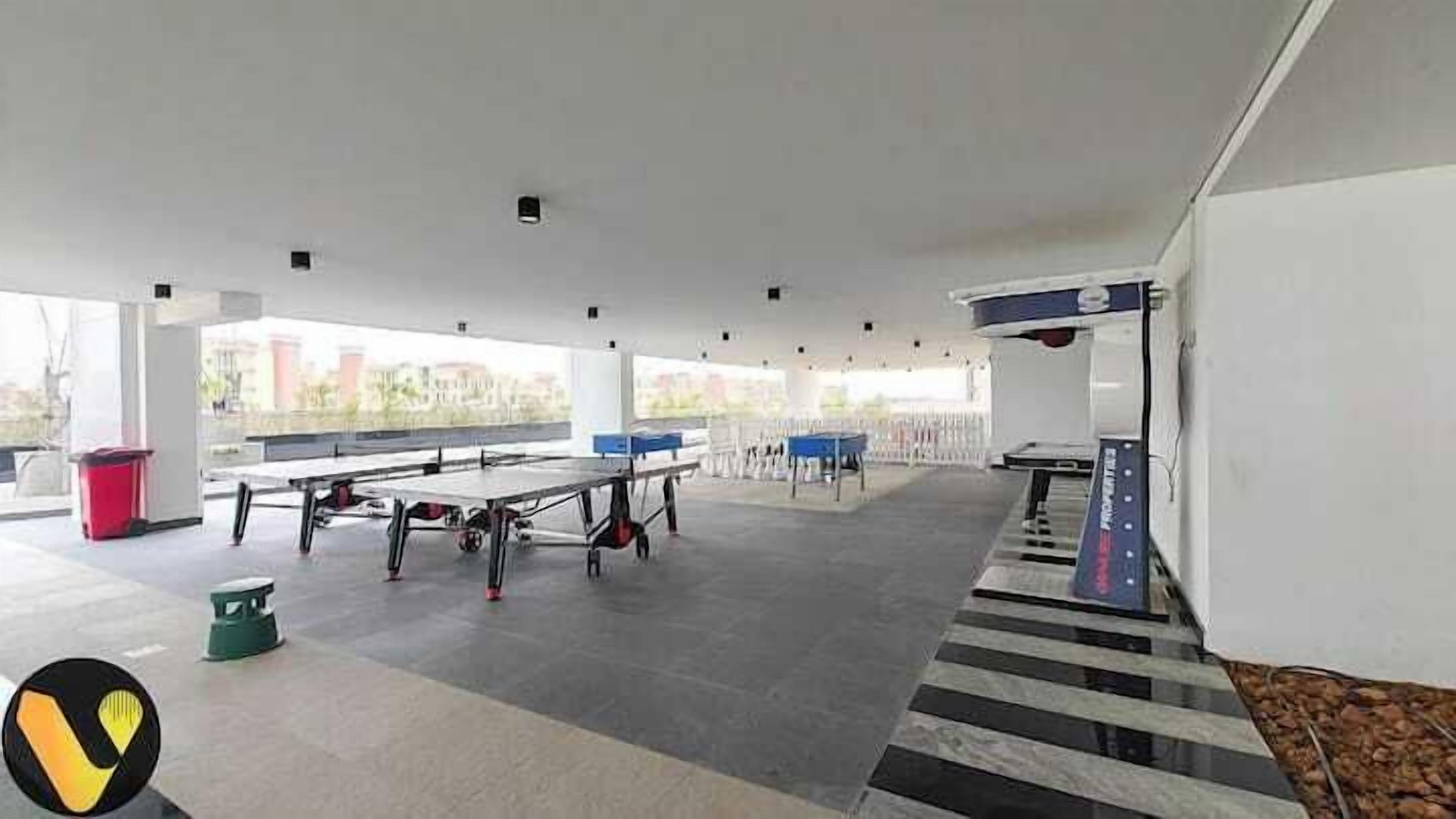 Amplio espacio interior con varias mesas de ping-pong, una escalera y vistas a edificios.
