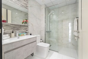 Un baño moderno con ducha de vidrio, tocador de mármol y retrete.