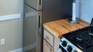 Una cocina con un refrigerador de acero inoxidable, armarios de madera, una estufa a gas y un florero con flores encima del refrigerador.