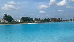 A clear blue sea with a sandy beach and a row of buildings in the background.