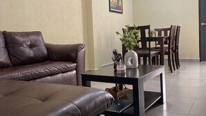 A living room with a brown leather sofa, a coffee table with decorative items, and a dining area with wooden chairs and a table.