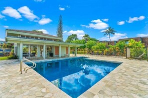 En swimmingpool med en terrass av sten, ett avskärmat sittområde och utsikt över ett bostadsområde.