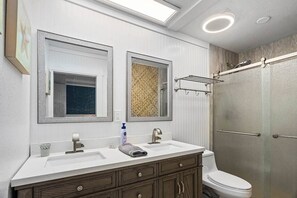 Ein Badezimmer mit weißem Waschtisch, zwei Spiegeln, einem Handtuch, einer Toilette und einer Duschkabine.