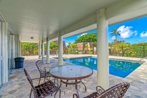 Ein überdachter Außenbereich mit Pool, Steinböden und Metallstühlen.