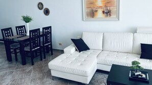 Een woonkamer met een witte bank, een eettafel met stoelen en een schilderij aan de wand.