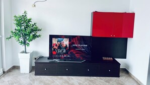 Een moderne woonkamer met een flatscreen televisie, een rode kast, een potplant en een luchtverkoeler aan de muur.