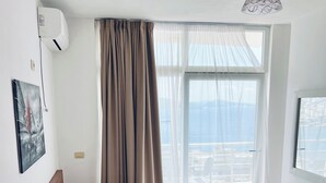 Een slaapkamer met een bed, een nachtkastje, een wandairconditioner, een schilderij en een raam met gordijnen.