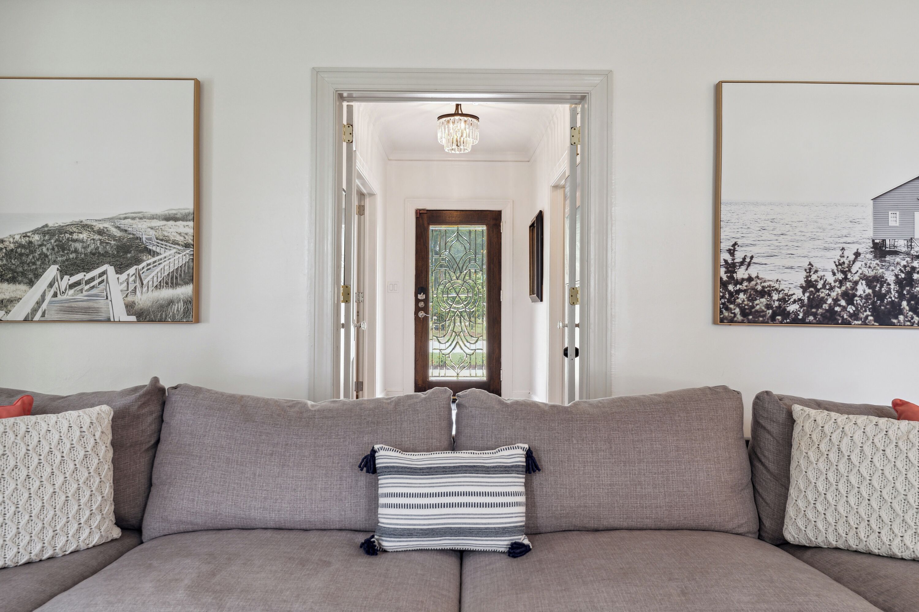 Un salon avec un canapé gris, un coussin à rayures et deux tableaux encadrés accrochés aux murs.