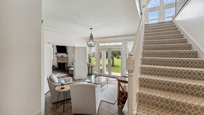 Een ruime woonkamer met een trap naar een balkon, een glazen salontafel en uitzicht op de omgeving.