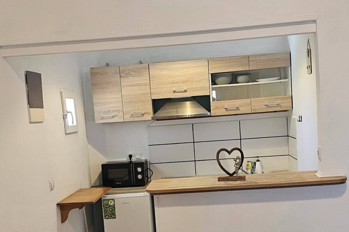 A compact kitchen with wooden cabinets, a microwave, a small refrigerator, and a heart-shaped decoration on the wall.
