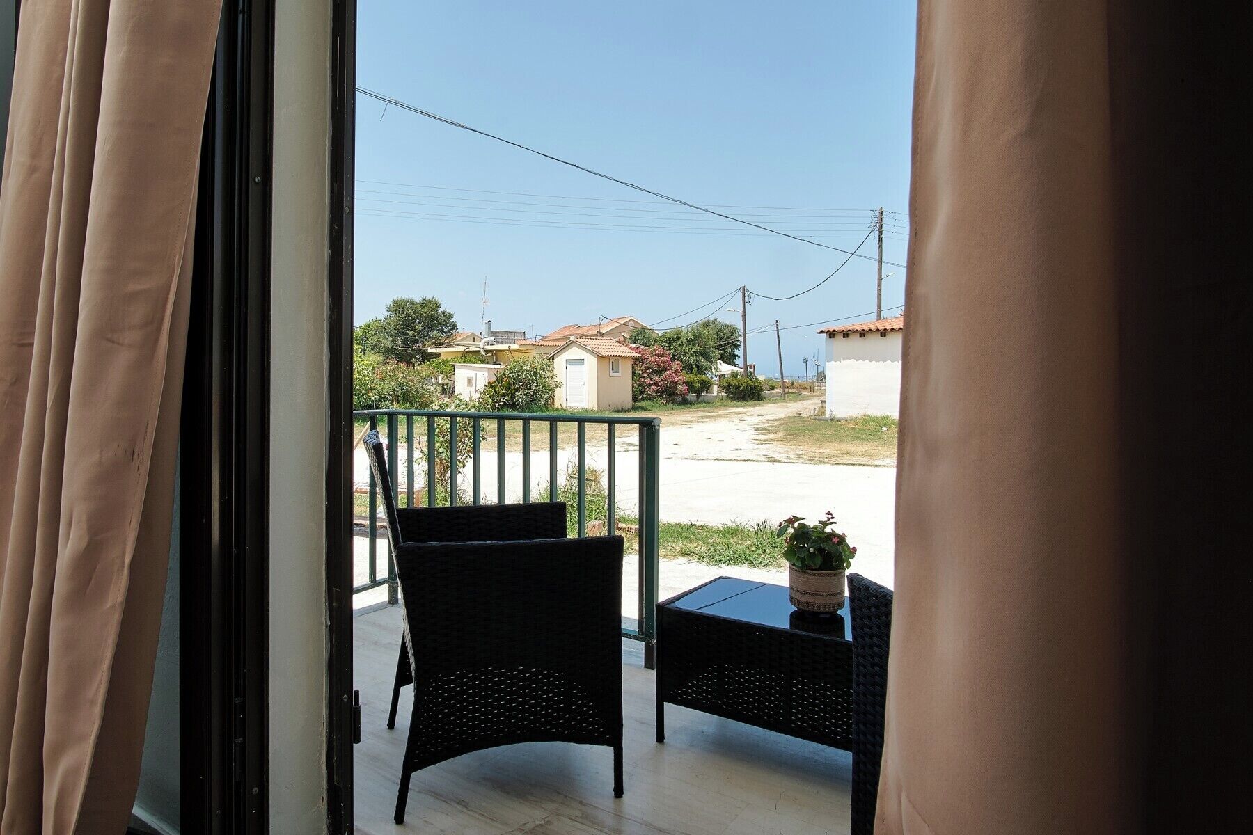 A balcony with wicker furniture and a potted plant, overlooking a residential street.