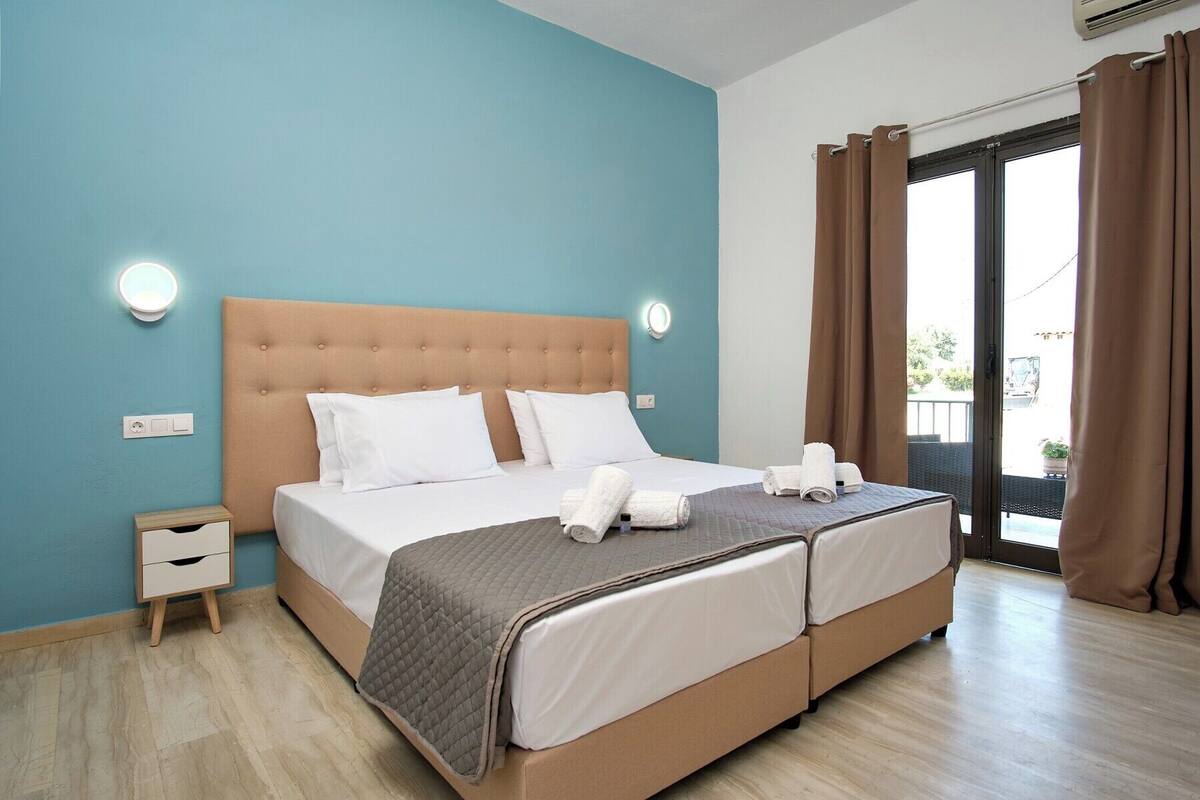 A double bed with a headboard, two bedside tables, a window with curtains, and a view of the outside.