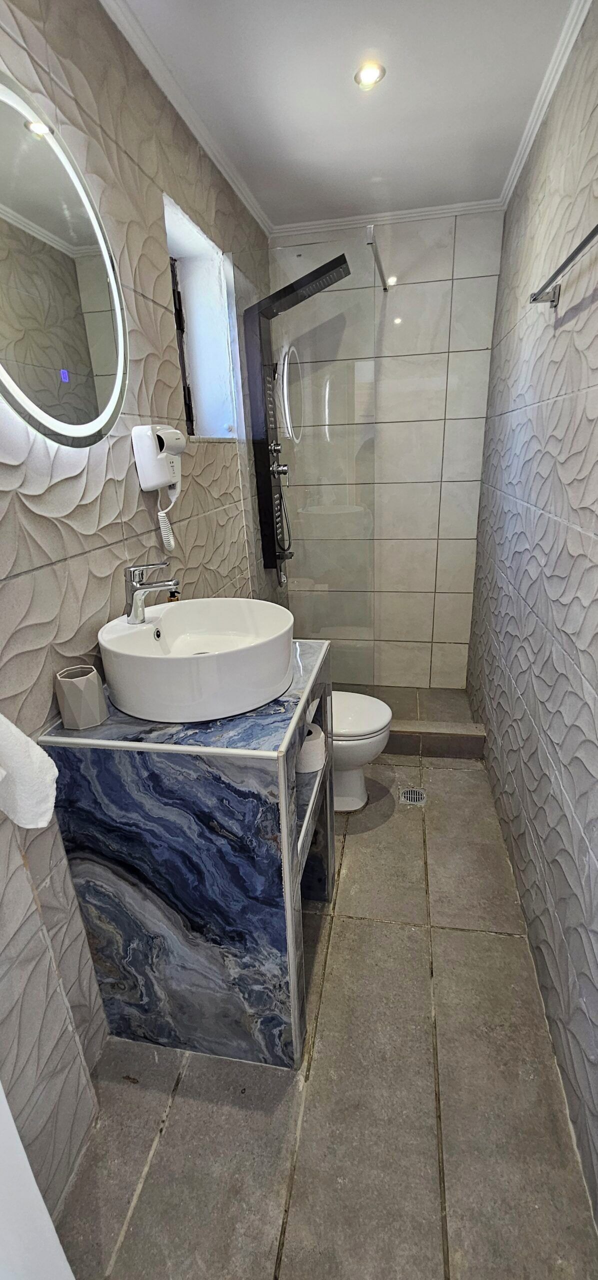 Une salle de bain avec un lavabo en marbre, des toilettes, une douche et un miroir.