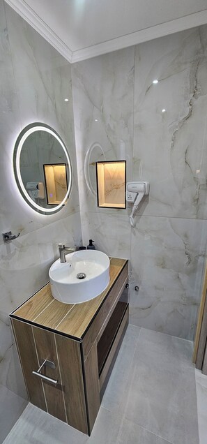 A modern bathroom with a marble wall, a wooden vanity, a round mirror with a light, and a hairdryer on the wall. - Sidari Escapes By The Beach (Corfu)