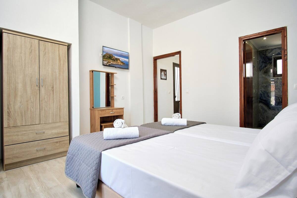 A bedroom with a bed, a wooden wardrobe, a vanity with a mirror, and a painting on the wall.