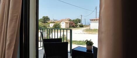 A balcony with two wicker chairs and a small table, overlooking a residential area with houses and a clear sky.