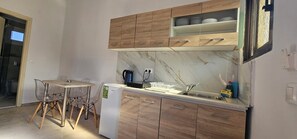 A compact kitchen with wooden cabinets, a marble backsplash, a small dining table with chairs, and a compact refrigerator.