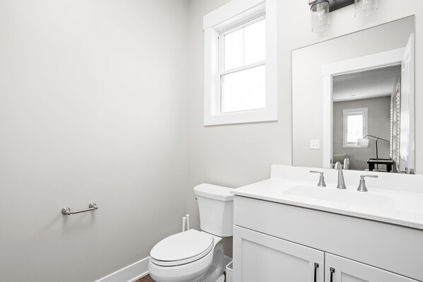 A modern bathroom with a white toilet, a sink with two faucets, and a large mirror above the sink.