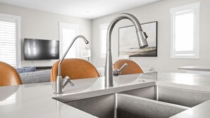 Una cocina moderna con un lavamanos doble, grifo de acero inoxidable y un televisor de pantalla plana al fondo.