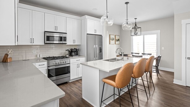 Una cocina moderna con armarios blancos, electrodomésticos de acero inoxidable y una isla central con taburetes de bar.
