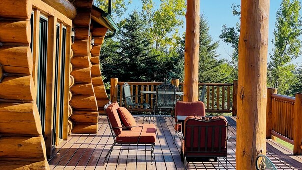 A wooden deck with a covered seating area, including a sofa and chairs, and a view of the surrounding trees. - Foote Creek Lodge (Aberdeen)