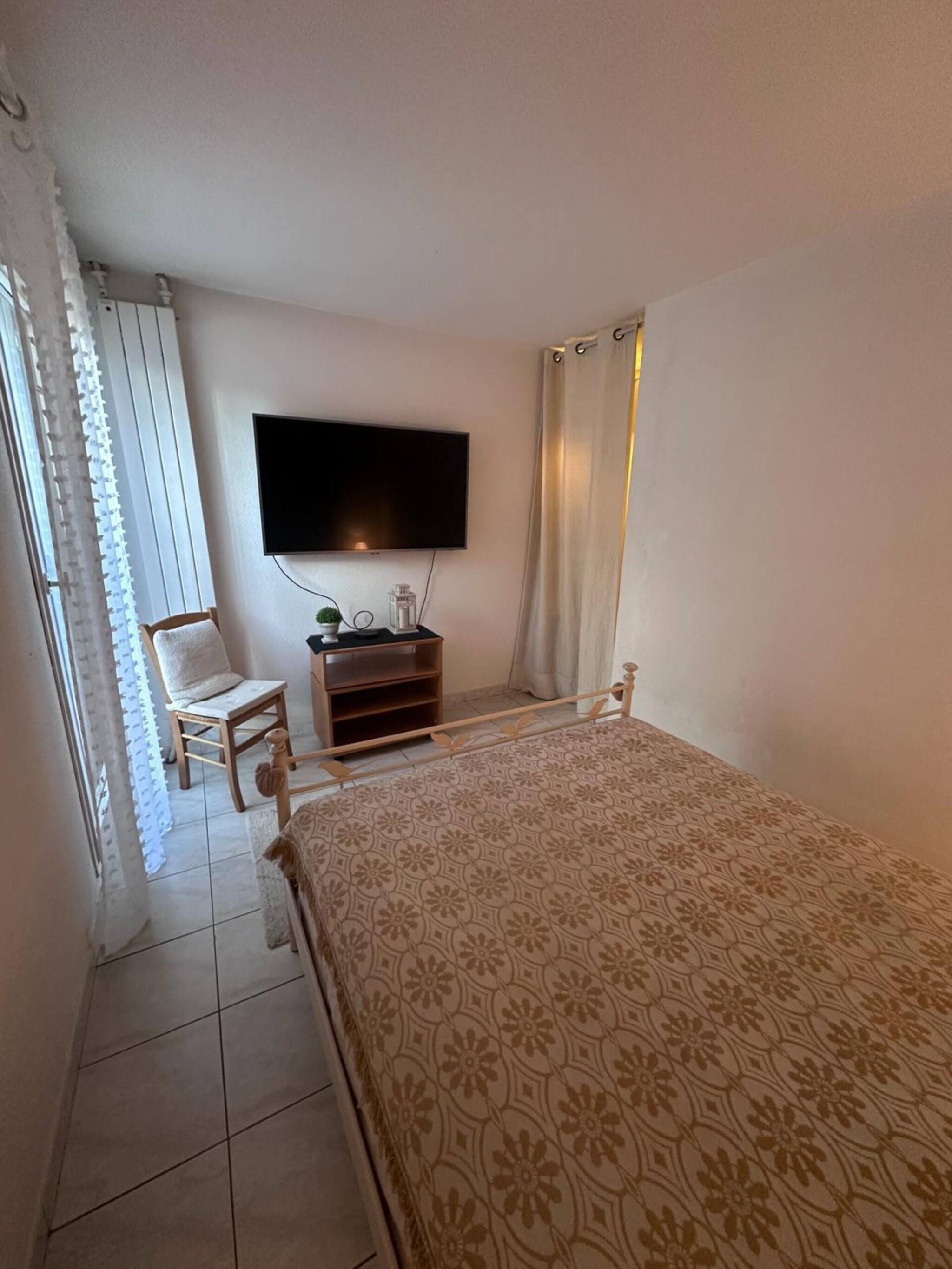 Une chambre à coucher avec un lit, un téléviseur fixé au mur, une chaise et une petite table sur laquelle se trouve une plante.