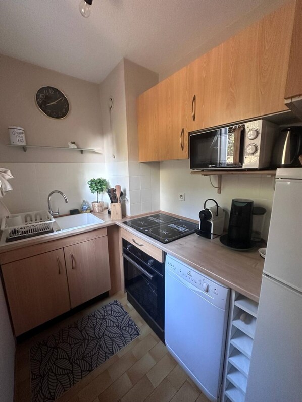 A compact kitchen with wooden cabinets, a microwave, a coffee maker, a dishwasher, and a sink. - Apartment right on the beach (Saint-Raphaël)