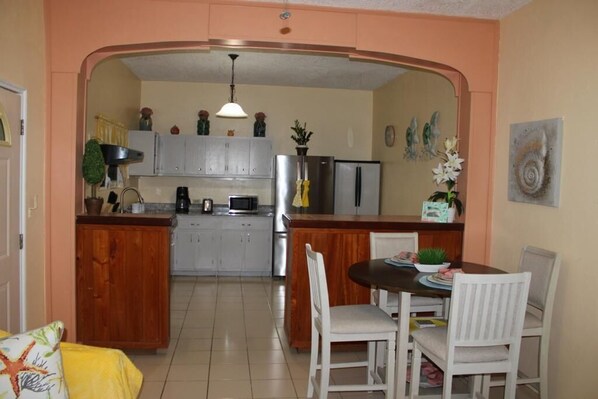 Una cocina con una isla central, sillas blancas y una mesa de comedor.