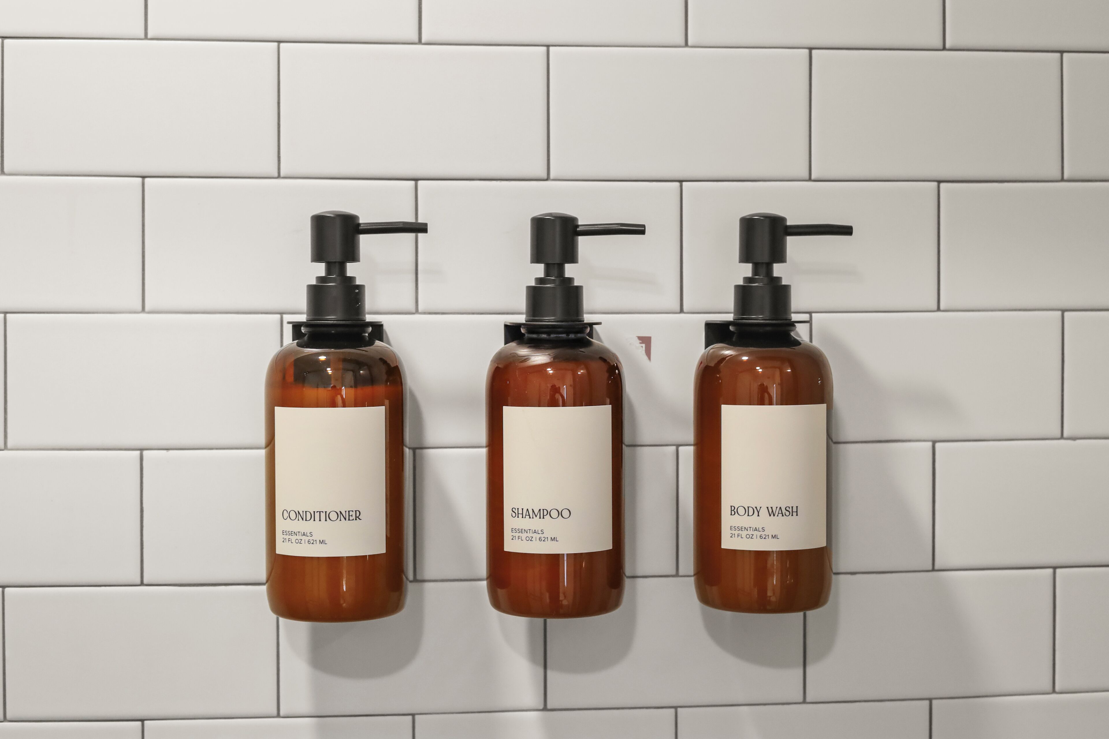 Three bottles of toiletries on a tiled wall.