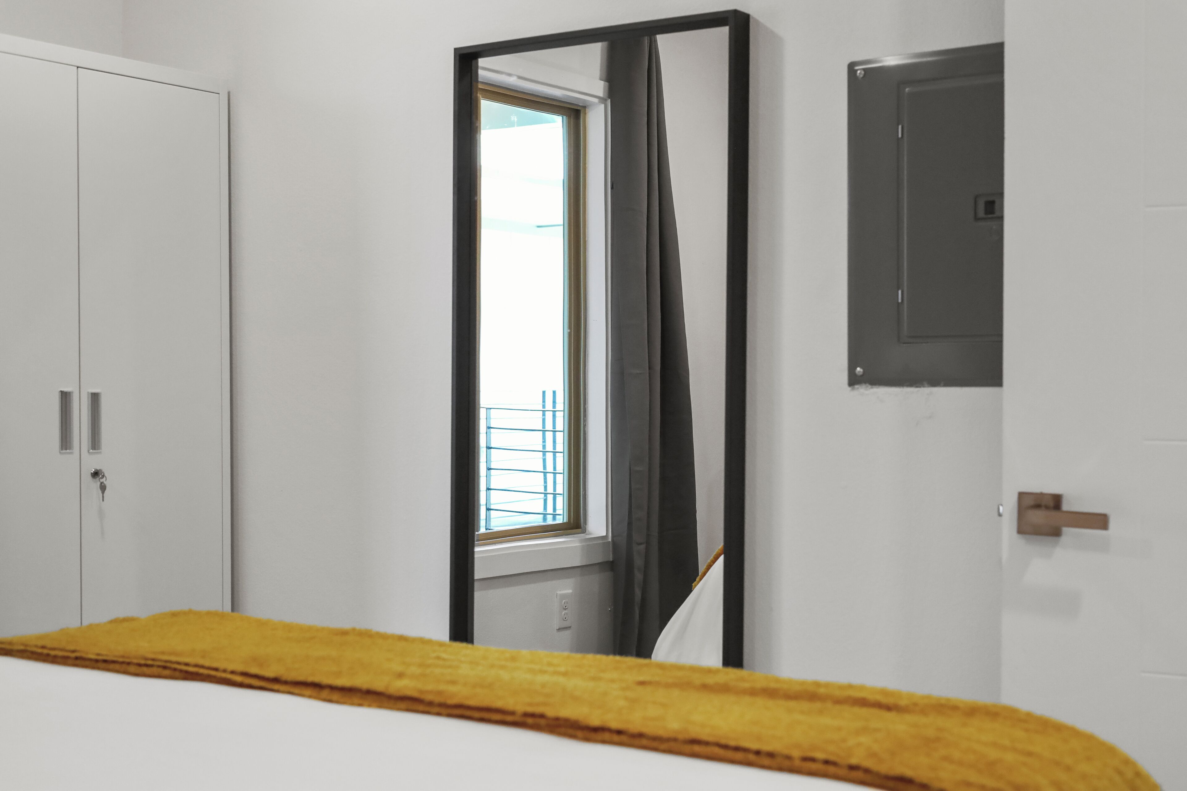 A bedroom with a bed, a wardrobe, a window with blinds, and a door with a handle.
