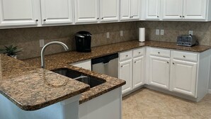 A kitchen with white cabinets, granite countertops, and a dishwasher.