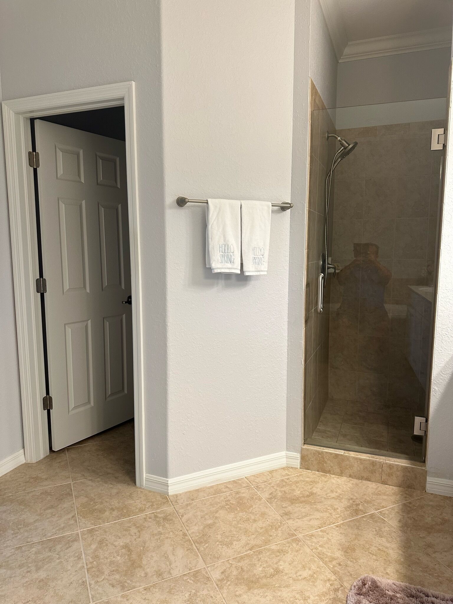A bathroom with a glass shower enclosure, a towel rack with two towels, and a door leading to another room.