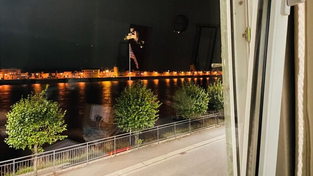 A nighttime view of a river with buildings on the opposite bank, a metal railing, and a tree-lined sidewalk. - Rheinromantik mit Blick auf die Burg Katz, bis 4P (Sankt Goar)
