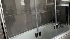 Uma casa de banho moderna com chuveiro em cabine de vidro, uma banheira branca e uma área de lavatório visível.