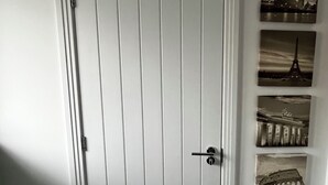 Uma porta branca com painéis verticais, uma maçaneta e uma fechadura. À direita, há três quadros com imagens de pontos turísticos famosos.