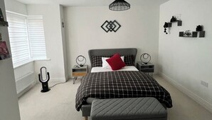 Quarto com uma cama, mesa de cabeceira, abajur e prateleira na parede.